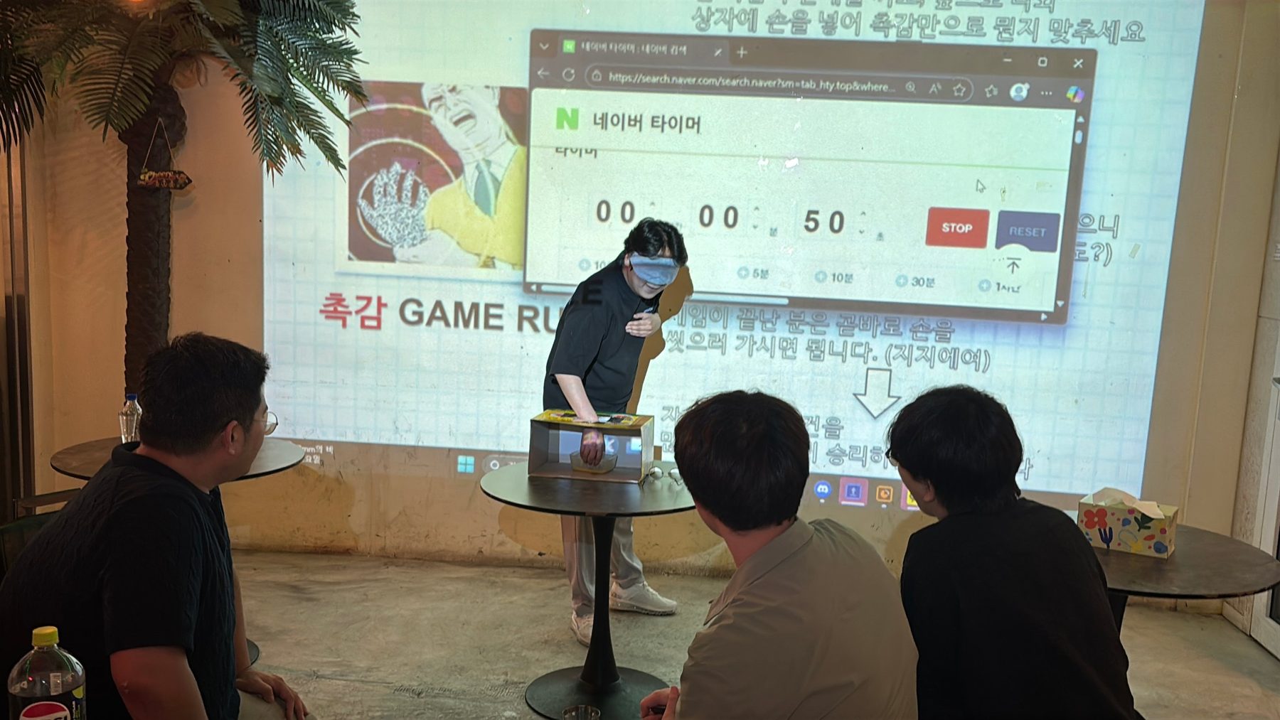 워크숍 게임 중 상자에 손을 넣어 물건을 맞히는 직원